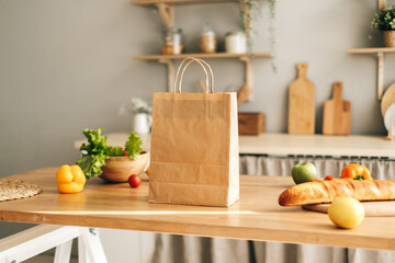 Fototapeta na wymiar Eco shopping paper bag with fresh vegetables and baguette on the table in modern kitchen. Food delivery or market shopping concept.