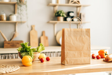 Eco shopping paper bag with fresh vegetables and baguette on the table in modern kitchen. Food delivery or market shopping concept.