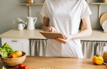 Caucasian woman use tablet computer in the modern kitchen, preparing salad, read recipe.