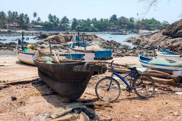 Old wooden fishing boats and bike on the sandy shore of the Indian ocean, with the tree and stones