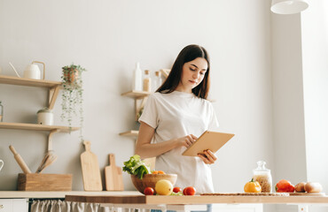 Young caucasian woman use tablet computer in the modern kitchen, preparing salad, read recipe.