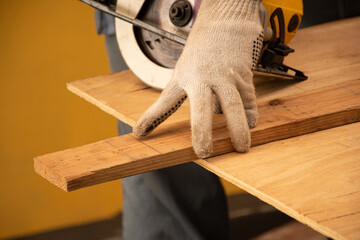 Selective focus. The carpenter push a part of wooden board out of the table. He prepare to cut the plank with an electronic saw. A carpenter works on a wooden table.