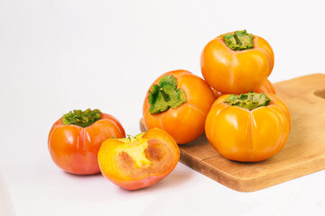 Ripe persimmon fruits isolated on wooden cutting board, Diospyros kaki wholes and half, white background