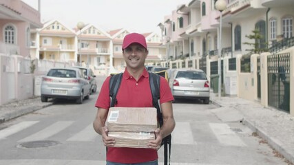 Friendly male courier with thermal backpack holding packages, standing and posing outside, looking at camera and smiling. Medium shot, front view. Shipping or delivery service concept