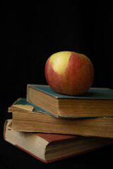 red apple on a stack of old books on a black background