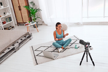 Young woman using DSLR camera for live streaming teach yoga online in living room.