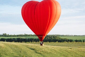 Hot air balloon in shape of heart is landing on the green field