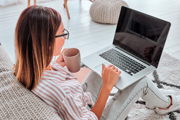 Woman sitting on floor holding a coffee mug working on laptop computer.