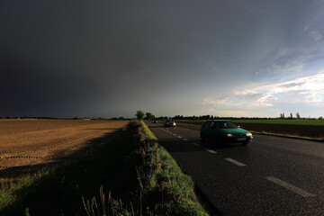 Fototapeta na wymiar Samochody na drodze asfaltowej pośród póli na tle pochmurnego nieba.