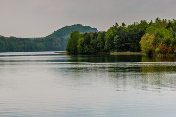 Lake with its calm waters and reflection surrounded by abundant trees and green vegetation, cloudy day with a gray sky in Maasmechelen Belgium.  Inspiration and meditation in a magical place