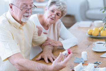 Elder man reading a label of a drug sitting next to his worried wife