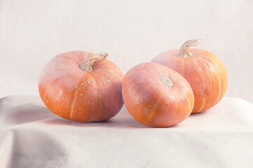 Three small pumpkins are on a white linen background with fog.