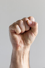 Male hand showing raised fist on gray background.