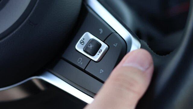 Man pushes the navigation buttons of the on-board computer on the steering wheel of a car.