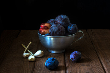Plums and garlic in a metal bowl. Moonlight.