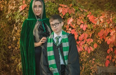 Kid and witch woman in of the magical atmosphere. Boy and mom in green robe magic in the forest. Family Halloween time