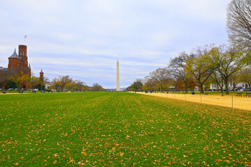 National Mall in autumn with the Washington Monument at distance in Washington DC, USA. The National Mall landscape with empty benches and historic buildings on both sides under cloudy skies.