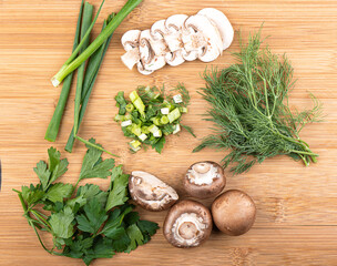 Top view. Sliced and whole mushrooms, green onions, parsley and dill on a wooden background. Chopped greens in the center.