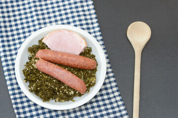 Fresh cooked kale with sausages, meat and wooden spoon  in the pan on black background