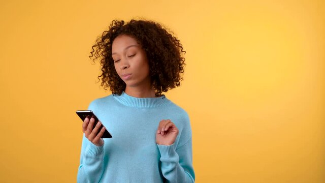 puzzled young woman on a yellow background touches her chin and looks into a smartphone. The woman makes a choice between several plaques. Isolated on a bright yellow background. 4K