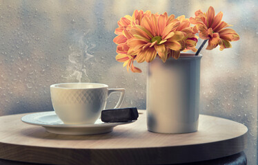 Obraz na płótnie Canvas White coffee cup with smoke, vase with orange flowers on table in cafe