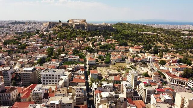 Aerial tilt down shot of beautiful Acropolis monument on hill and old city of Athens during hot summer day.