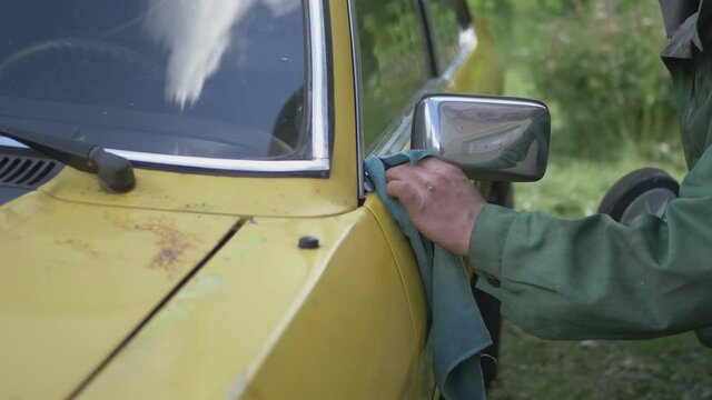 A Man Cleans A Polished Yellow Vintage Car Side Mirror