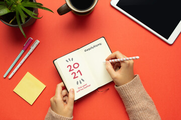 Stock photo of woman's hand writing resolutions in a 2021 new year notebook on red background