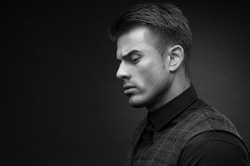 Black and white portrait of beautyful guy on dark background. High fashion model posing in studio. Attractive man in classic suit.