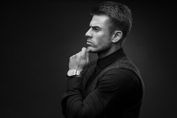 Black and white portrait of beautyful guy on dark background. High fashion model posing in studio. Attractive man in classic suit.