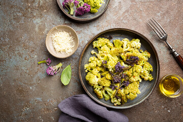 Fried green and purple cauliflower with herbs and spices on plate over gray stone background. Top view