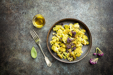 Fried green and purple cauliflower with herbs and spices on plate over gray stone background. Top view