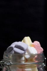 Marshmallows of different colors. They lie in  glass jar. Photographed close-up on a black background.