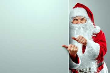 Portrait of Santa Claus in a red suit points his fingers, light background. Concept for christmas eve, vacation, holiday banner, new year.