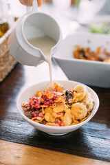 Soy milk pouring in acai bowl mix with fresh mango, avocado, banana, berries, sunflower seeds, chia seeds and cereal. Superfood breakfast bowl for healthy and vegan people.