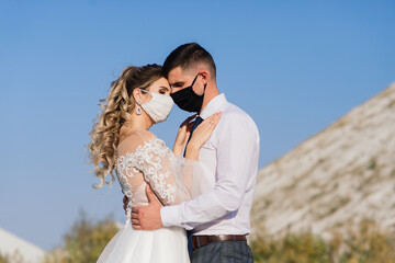 Young loving couple in medical masks in park during quarantine on wedding day.