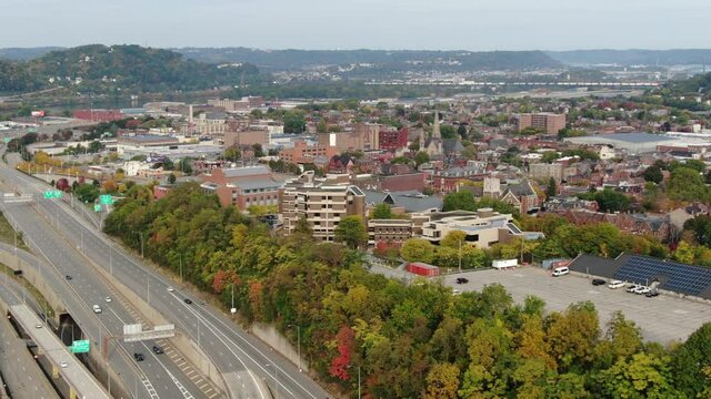 Aerial pan of Pittsburgh PA USA neighborhood, Route 65, Chateau, Manchester, Old Allegheny Rows Historic District, autumn fall foliage dots skyline. Train crosses Ohio River in distance.