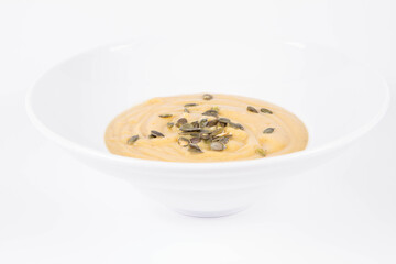 Pumpkin soup decorated with pumpkin seeds on a plate  on a white background