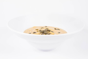 Pumpkin soup decorated with pumpkin seeds on a plate  on a white background