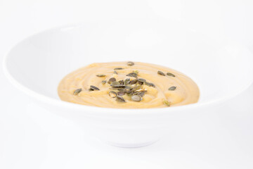 Pumpkin soup decorated with pumpkin seeds on a plate  on a white background
