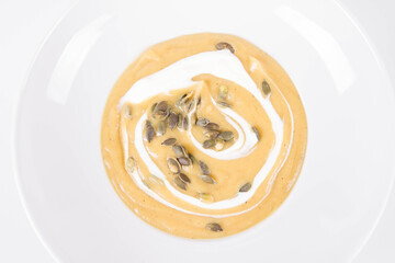 Pumpkin soup decorated with cream and pumpkin seeds on a plate  on a white background