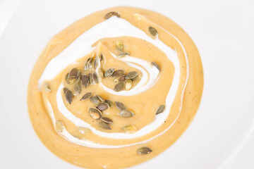 Pumpkin soup decorated with cream and pumpkin seeds on a plate  on a white background