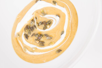 Pumpkin soup decorated with cream and pumpkin seeds on a plate  on a white background