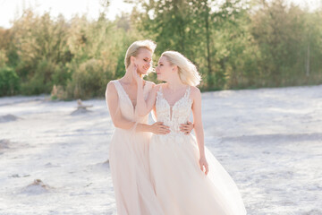 Fototapeta na wymiar Beautiful lesbian couple walking on sand along river bank on their wedding day