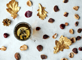 Fototapeta na wymiar a cup of tea with lemon slice, chestnuts and golden leaves. Natural decorative background.