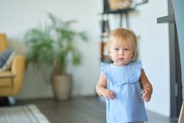 Portrait of a pretty little baby girl in a blue dress. cute blonde babe in the living room