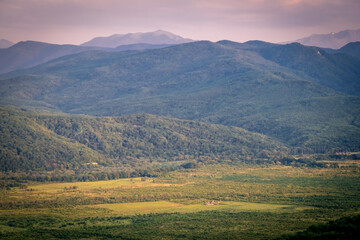 Early morning in the mountains. Morning sun and haze in the valley against the background of mountains. Green fields and meadows.