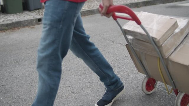 Deliveryman wheeling cart with parcels, walking down street. Closeup of legs and feet, cropped shot. Shipping or courier service concept