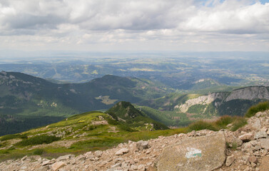View of the Tatras from the peak of Kasprowy Wierch. Summer day on the mountain trail. Greenery and rocks. Clouds and fog.