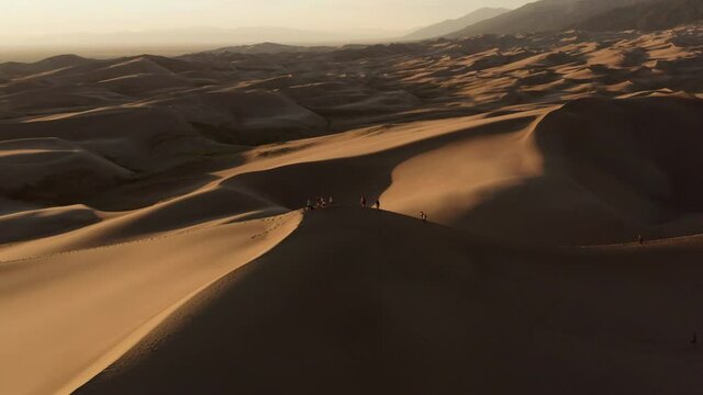 Aerial view away from a group of people on a dune, during sunset, in The great sand dunes national park, Colorado, USA - pull back, tilt drone shot